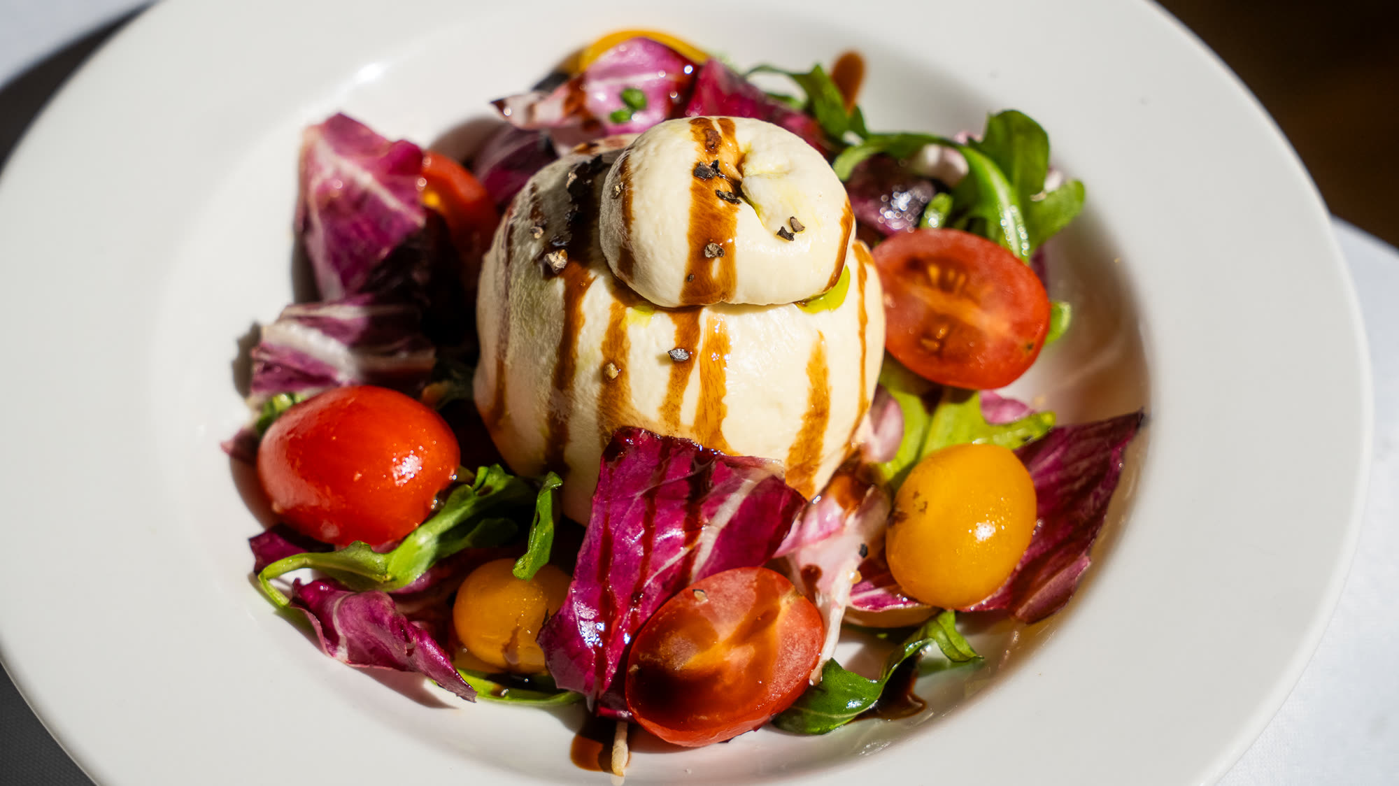 Close-up of a burrata salad with cherry tomatoes, radicchio and a balsamic drizzle.