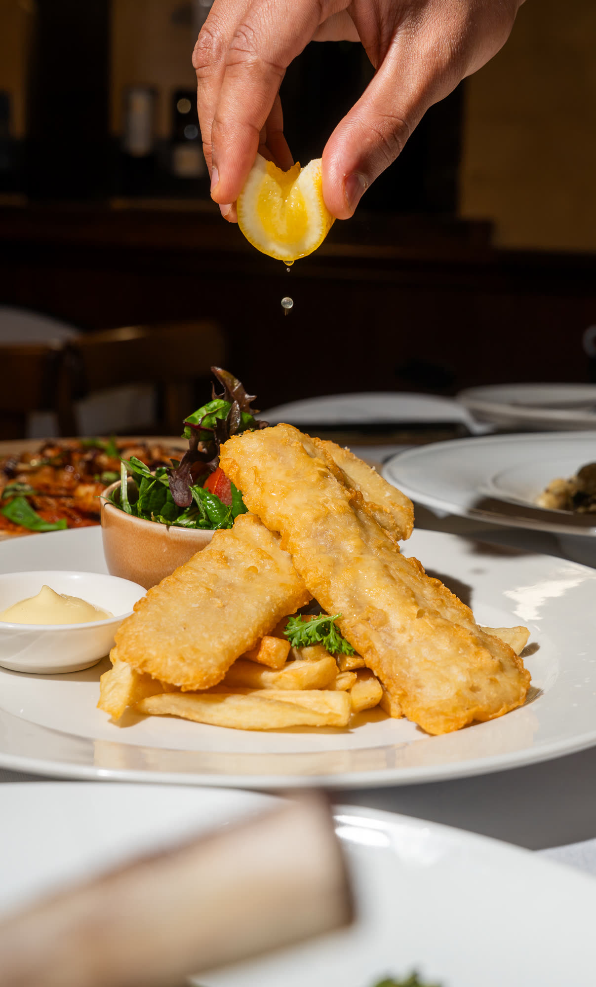 Beer-battered fish and chips with salad, with lemon being squeezed over the top.