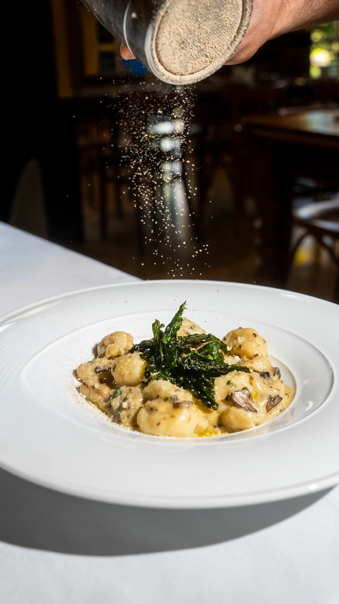 A plate of gnocchi with crisp greens, with black pepper being ground over the top.