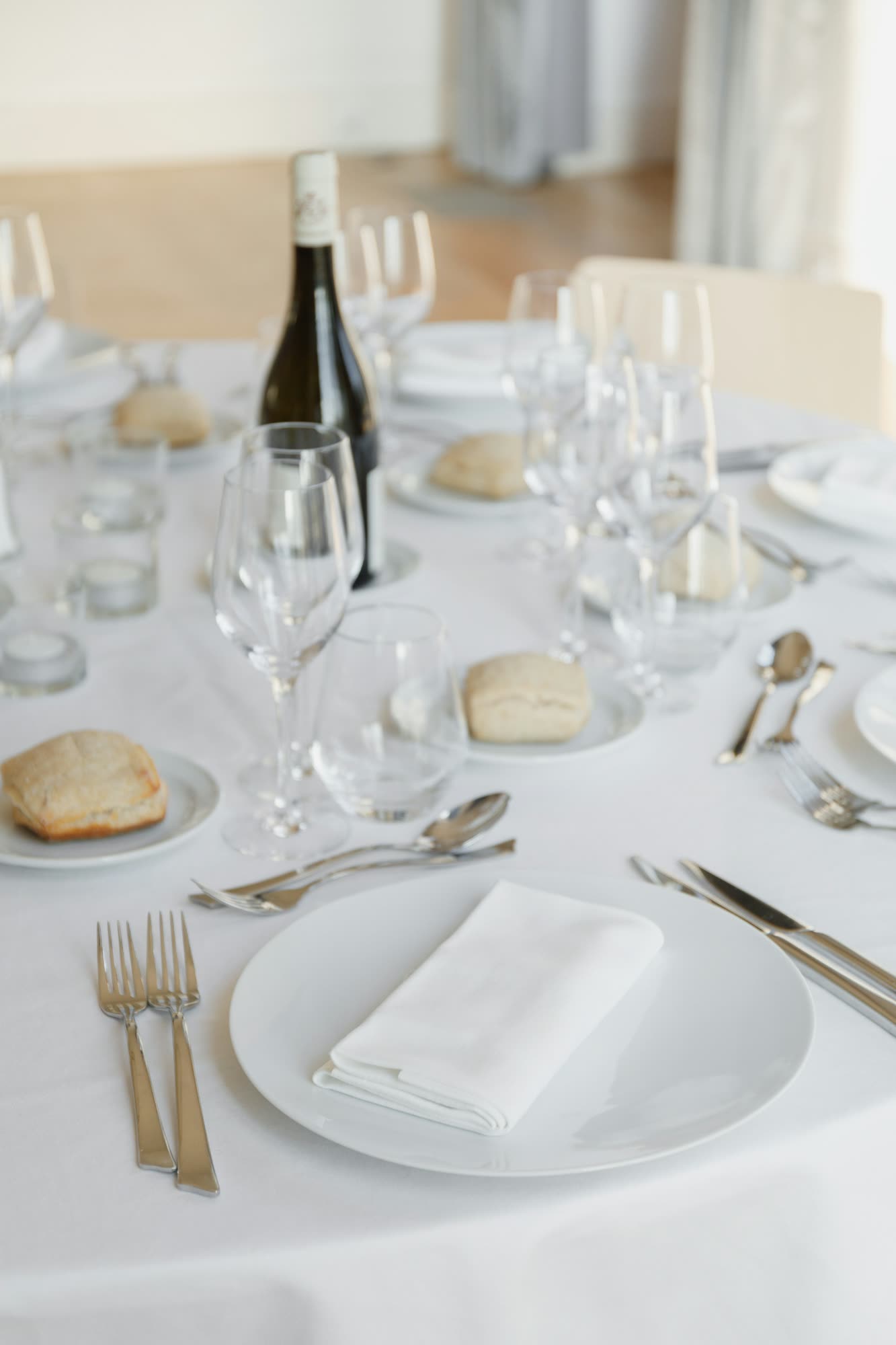 A white-linen place setting with plates, bread rolls and a bottle of wine, generic stock photo pending real venue photography.